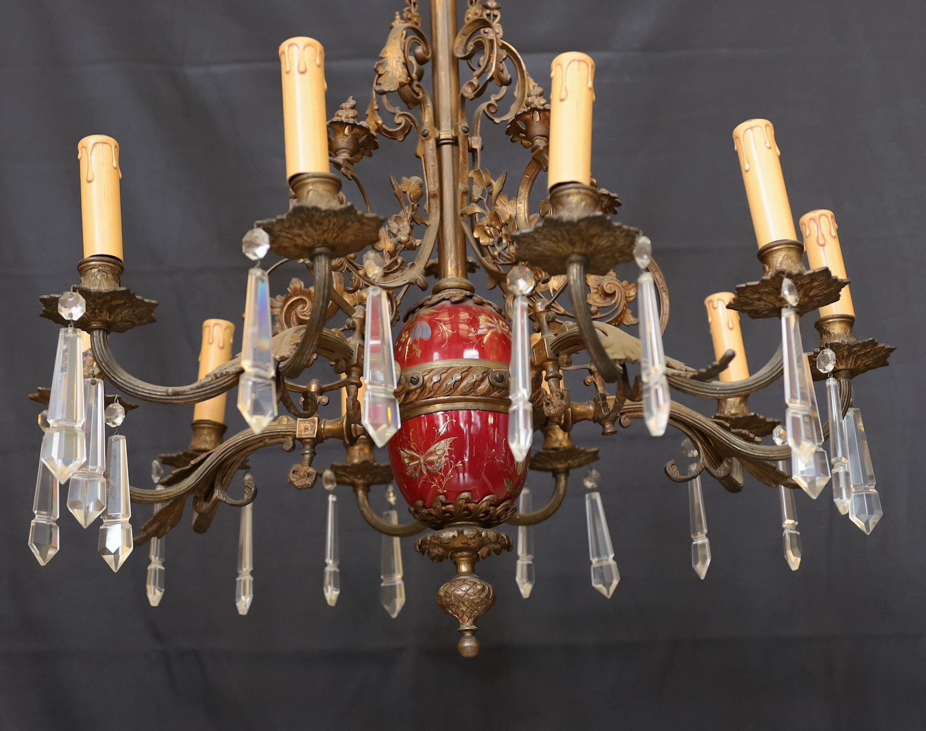 A Victorian bronze ten light gasolier with ornate scrolling foliate frieze and central ceramic stem, hung with spear shaped drops, later fitted for electricity, height 92cm. width 60cm